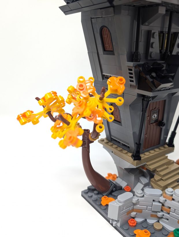 The autumn colors of the tree contrast the grey colors of the house.